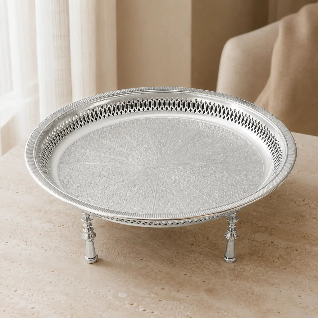 Zilverkleurig dienblad op pootjes op een lichte tafel in een beige interieur