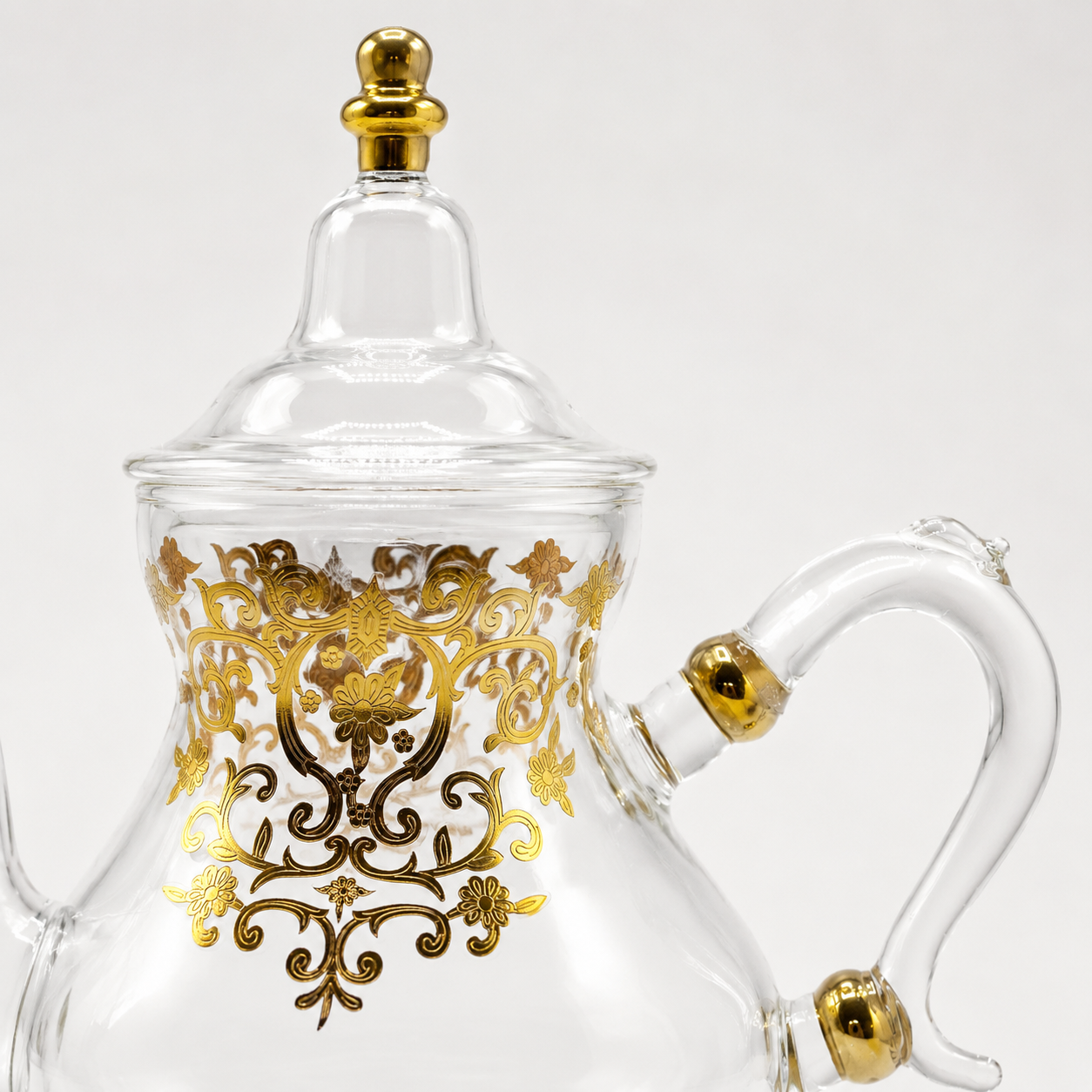 Detail van het goudkleurige ornament en glazen handvat van theepot Ifran